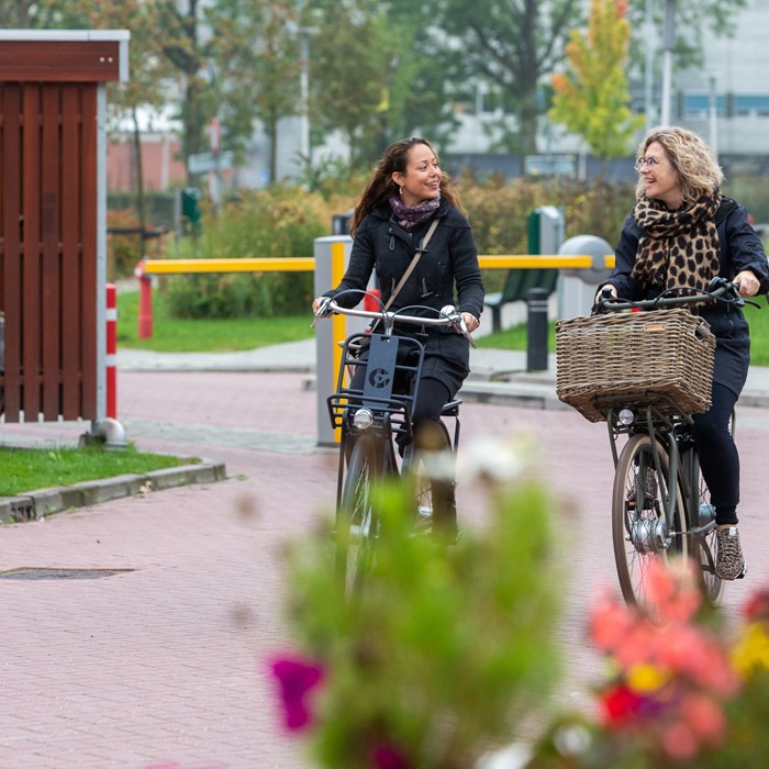 Twee medewerkers in gesprek op de fiets bij de fietsenstalling.