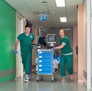 Twee verpleegkundigen met medisch apparatuur in de gang van de Intensive Care.