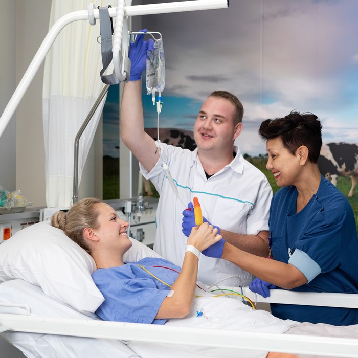 Patiënt in bed krijgt ijsje van twee verpleegkundigen.