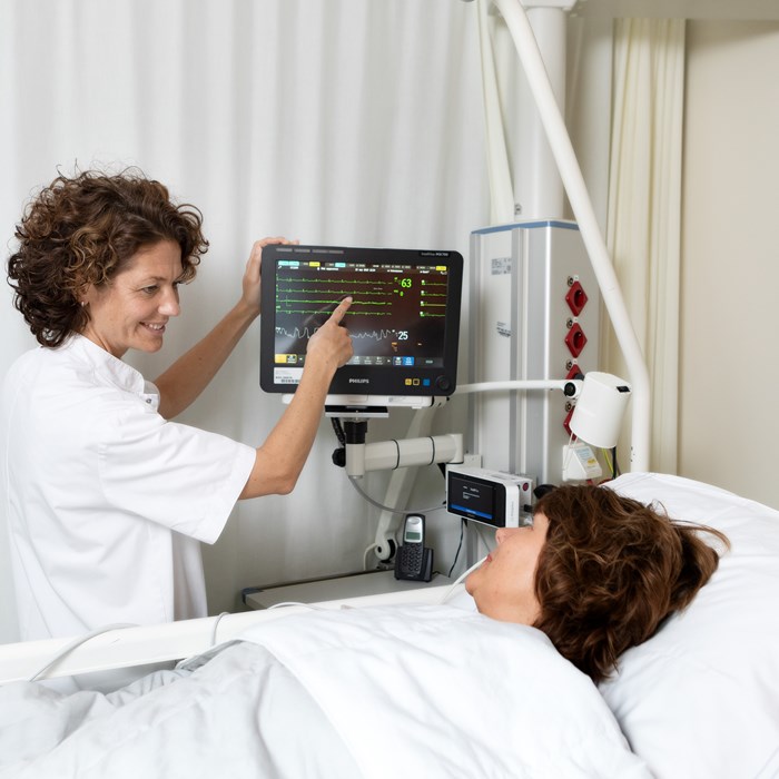 Verpleegkundig specialist laat cardiomonitor zien aan patiënt in bed.  