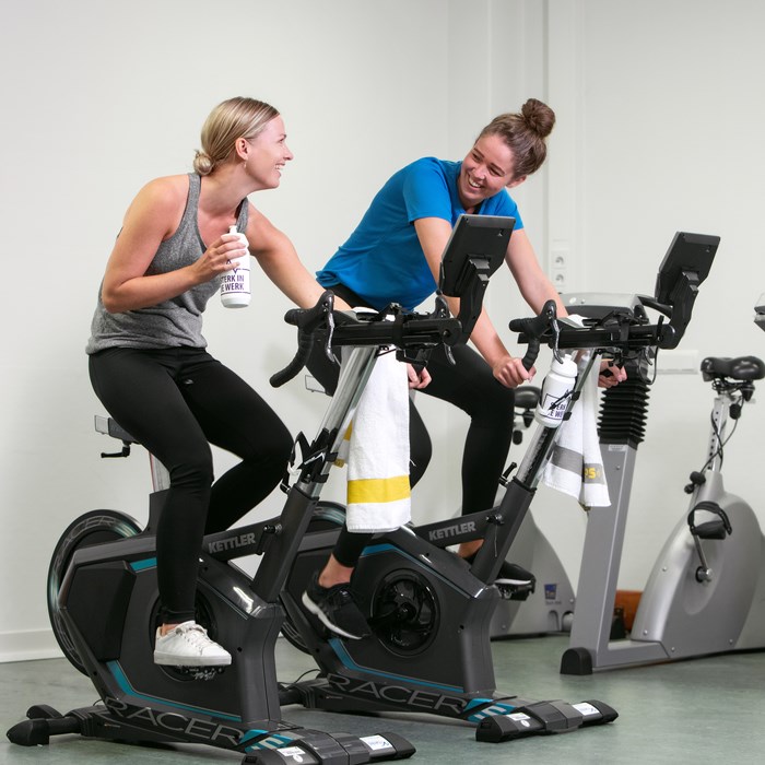 Twee medewerkers fietsen op hometrainers op de afdeling Fysiotherapie.