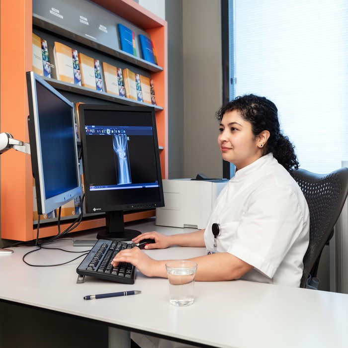 Arts bekijkt op de computer een röntgenfoto van een pols. 